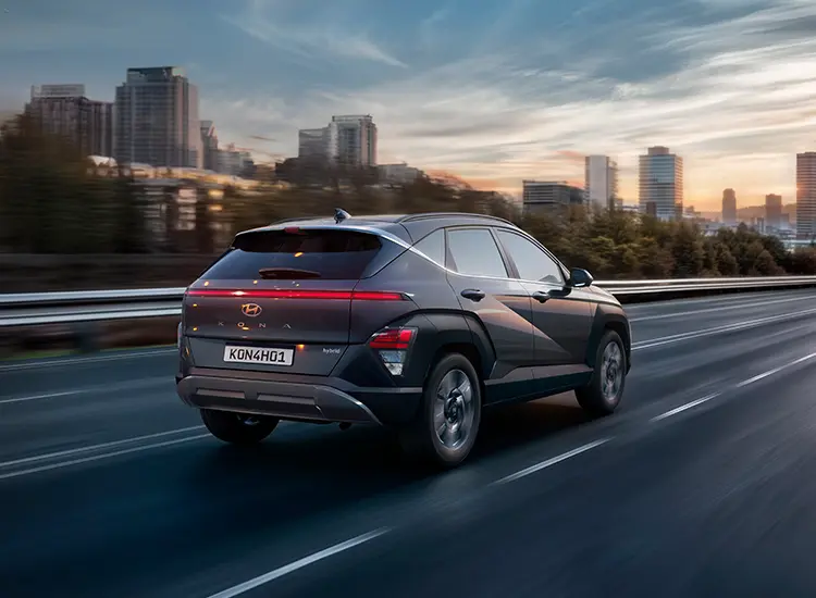 Novo Kona Hybrid na estrada com uma cidade ao fundo.