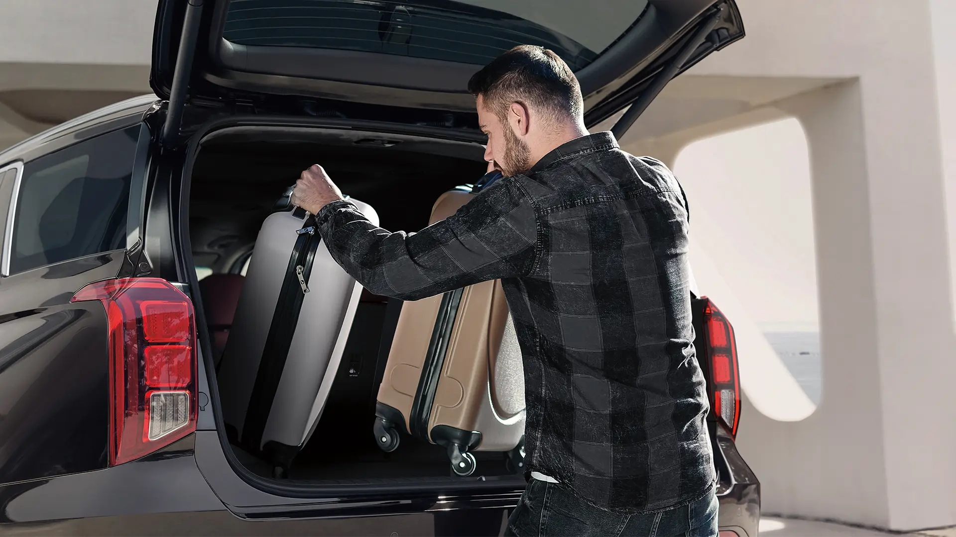 A imagem mostra um homem retirando malas do porta-malas de 704 litros do Hyundai PALISADE.