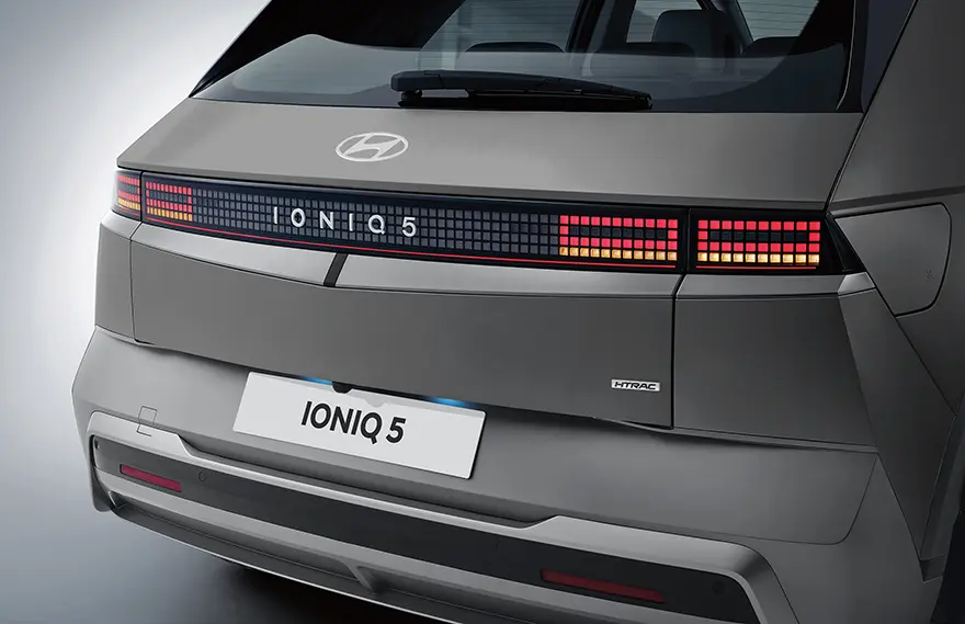 Visão traseira do IONIQ 5 na cor cinza com lanternas acesas e logo da Hyundai destacado.