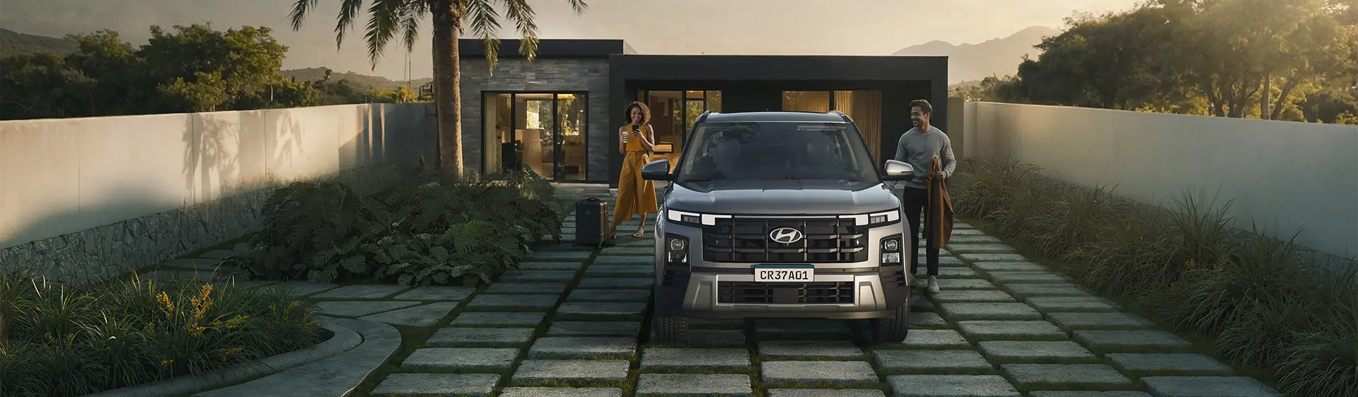 Modelo CRETA Platinum na cor cinza estacionado em uma casa durante o dia com casal ao lado.