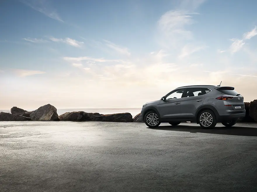 Modelo Tucson na cor cinza estacionada em um morro durante o dia com praia ao fundo.